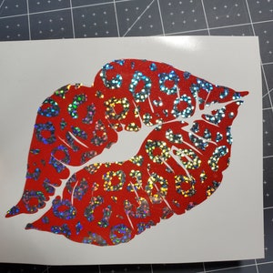 May include: Red lips with a leopard print pattern, made of iridescent vinyl. The lips are outlined in white and have a glossy finish.