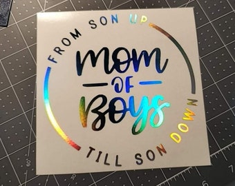 May include: A white sticker with a rainbow iridescent circle around the text "From son up, mom of boys, till son down".