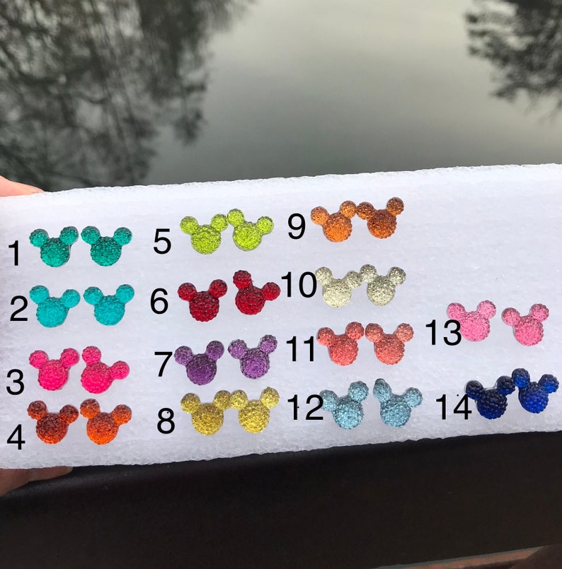 Puede incluir: Una tabla blanca con 14 dijes en forma de cabeza de Mickey Mouse de diferentes colores. Los dijes est&aacute;n numerados del 1 al 14. Los dijes est&aacute;n hechos de vidrio y tienen un acabado brillante.
