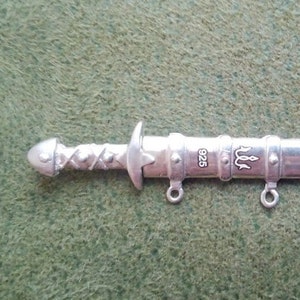 May include: Silver sword pendant with a braided handle, a trident symbol, and the inscription "925".