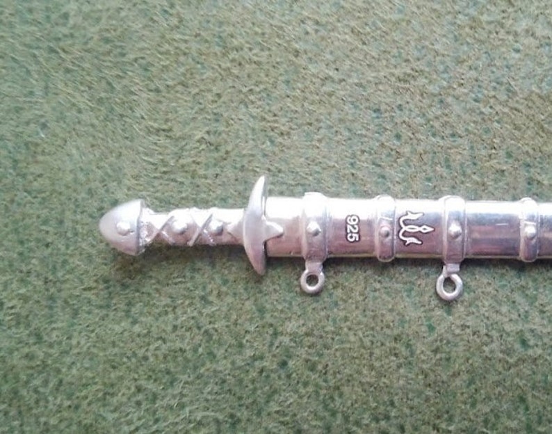 May include: Silver sword pendant with a braided handle, a trident symbol, and the inscription "925".
