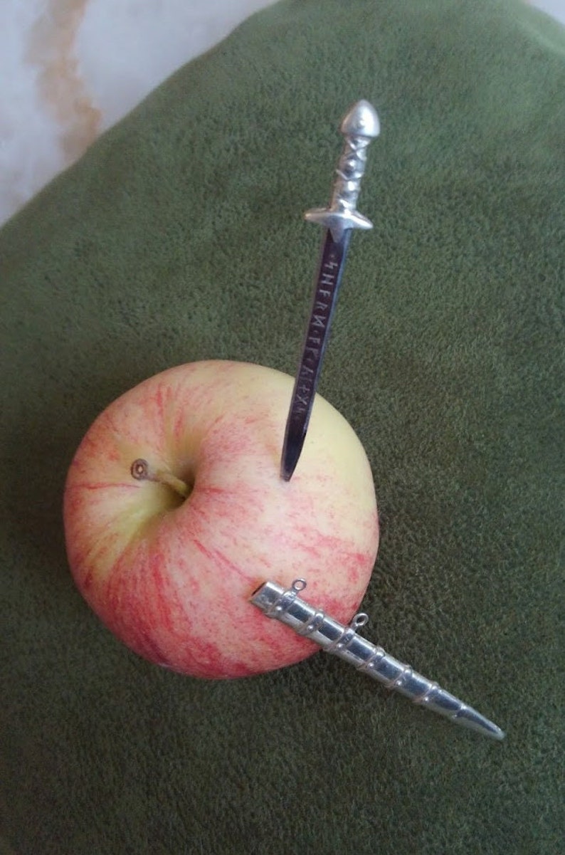 May include: A red and yellow apple with two silver swords sticking into it. The swords have intricate designs and one has the inscription "The Metal Era".