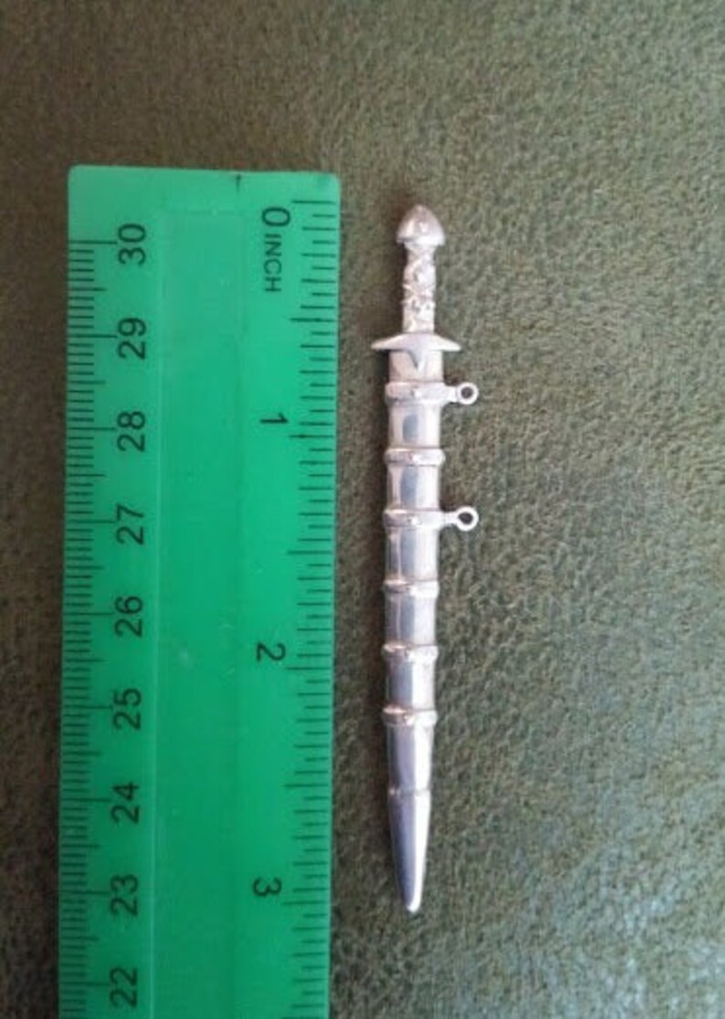 May include: A silver sword charm with intricate details, measuring approximately 2 inches in length.
