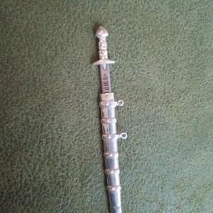 May include: A silver-colored, miniature sword with a detailed handle and a blade that reads "DIRK'S".