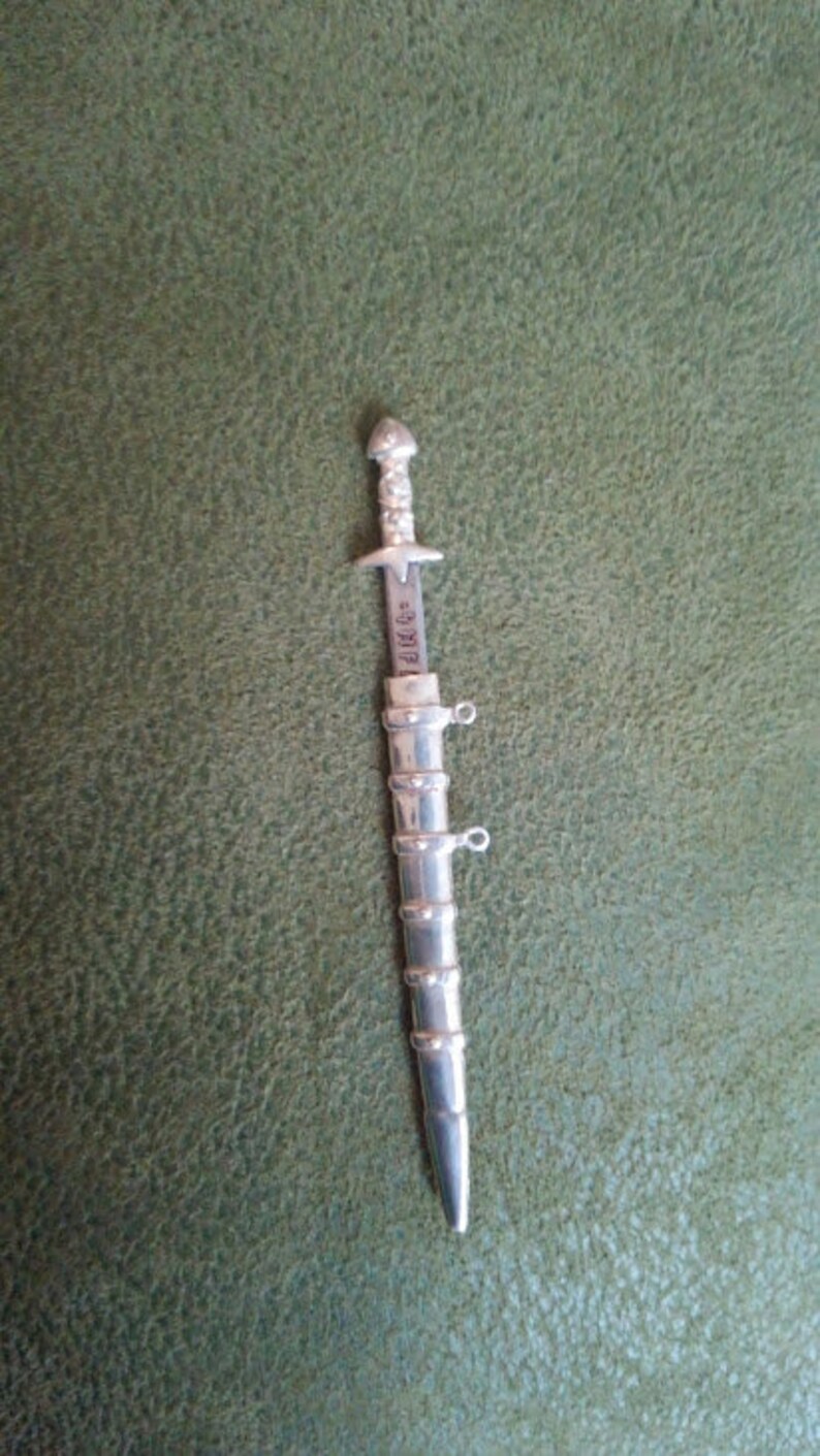 May include: A silver-colored, miniature sword with a detailed handle and a blade that reads "DIRK'S".