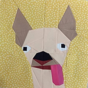 May include: A paper pieced quilt block featuring a dog with a pink tongue sticking out. The dog is made of beige, brown, black, and white fabric. The background is a yellow fabric with a white speck pattern.