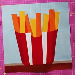 May include: A red and white striped paper container filled with orange and yellow french fries. The fries are arranged in a vertical stack.
