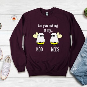 May include: Burgundy sweatshirt with a white graphic of two ghost bees. The text reads "Are you looking at my... BOO BEES".