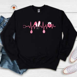 May include: Black sweatshirt with a pink Easter bunny and a pink heart with a nurse's cap and a caduceus symbol inside. The design is a heartbeat with a stethoscope on the left and a pink Easter egg on the right.
