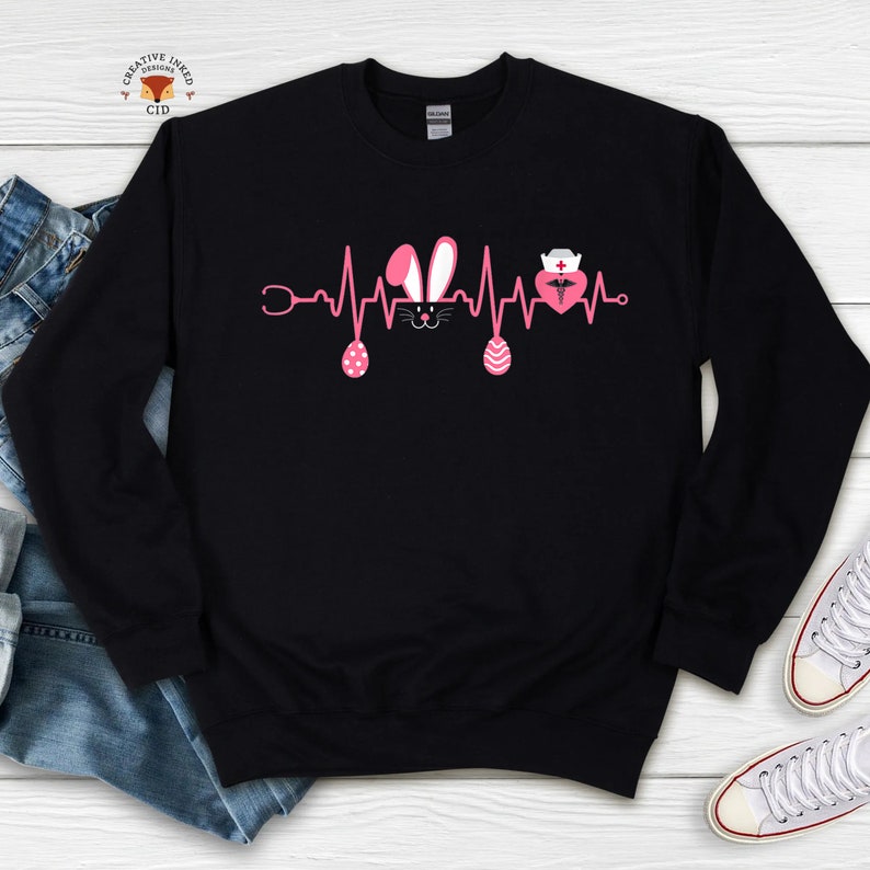 May include: Black sweatshirt with a pink Easter bunny and a pink heart with a nurse's cap and a caduceus symbol inside. The design is a heartbeat with a stethoscope on the left and a pink Easter egg on the right.