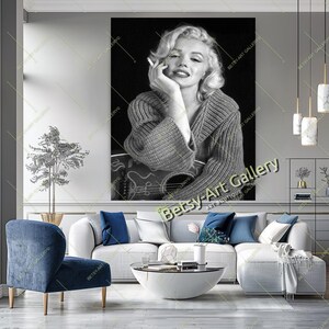 May include: Black and white portrait of Marilyn Monroe holding a cigarette and a guitar. She is wearing a sweater and smiling. The image is a print from Betsy-Art Gallery.