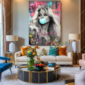 May include: A large canvas art print featuring a black and white portrait of a woman blowing a bubblegum bubble. The background has colorful graffiti and text. The artwork is displayed above a white sofa with colorful pillows.