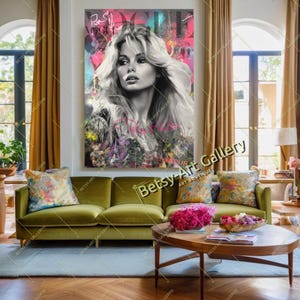 May include: A large, framed artwork featuring a black and white portrait of a woman with long, flowing hair. The background has splashes of pink, teal, and purple. The artwork hangs above a green velvet sofa with floral pillows.