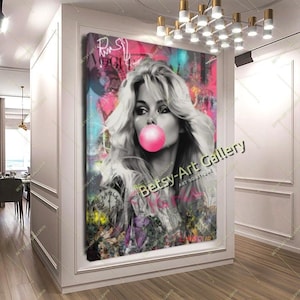 May include: A large canvas print featuring a black and white portrait of a woman blowing a pink bubblegum bubble. The background is a vibrant mix of pink, teal, and graffiti-style art. The print is displayed in a white-walled hallway.