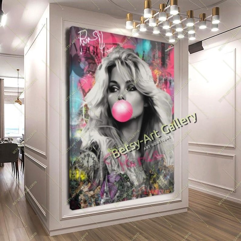 May include: A large canvas print featuring a black and white portrait of a woman blowing a pink bubblegum bubble. The background is a vibrant mix of pink, teal, and graffiti-style art. The print is displayed in a white-walled hallway.