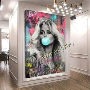 May include: A large canvas art print featuring a black and white portrait of a woman blowing a bubblegum bubble. The background is a vibrant mix of pink, teal, and graffiti-style text. The artwork is displayed in a modern hallway.