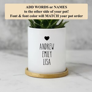 May include: White ceramic planter with a heart and the names Andrew, Emily, and Lisa written in black. The planter is sitting on a wooden base.