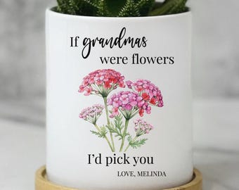 May include: A white cylindrical ceramic planter sitting on a circular bamboo tray. The planter features a watercolor illustration of pink flowers and black text that reads: If grandmas were flowers I'd pick you. LOVE, MELINDA. A green succulent plant is visible.