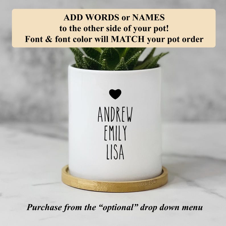 May include: A white cylindrical ceramic plant pot featuring a small black heart icon above the printed names ANDREW, EMILY, and LISA in a simple sans-serif font. The pot sits on a circular light brown wooden saucer and contains a green succulent.