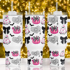 Op de afbeelding: Drie witte roestvrijstalen bekers met deksels en rietjes. Elke beker heeft een ander Halloween-thema met roze en zwarte accenten. De ontwerpen omvatten geesten, vleermuizen, spinnenwebben en pompoenen.