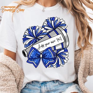 K&ouml;nnte beinhalten: Wei&szlig;es T-Shirt mit einer Grafik eines Megaphons, Pompons und einer Schleife in Blau und Silber. Das Megaphon hat ein Etikett mit der Aufschrift "Add your own text". Das Shirt ist ein l&auml;ssiger Stil.