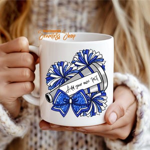 K&ouml;nnte beinhalten: Wei&szlig;e Keramik-Tasse mit einem Cheerleader-Design. Das Design umfasst blaue und silberne Pompons, ein Megaphon und eine Schleife. Das Megaphon hat ein Etikett mit der Aufschrift "Add your own text". Die Tasse wird von einer Person gehalten.