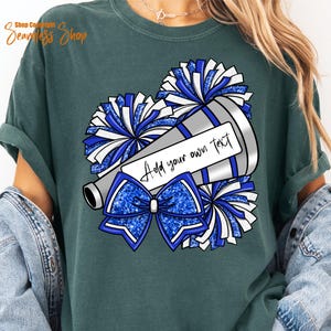 K&ouml;nnte beinhalten: Gr&uuml;nes T-Shirt mit einem Cheerleader-Design. Das Design zeigt ein Megaphon mit dem Text "Add your own text", blaue Pompons und eine blaue Schleife. Das Design ist in Blau-, Wei&szlig;- und Silbert&ouml;nen gehalten.
