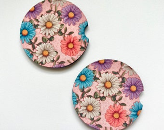 May include: Two round pink coasters with a floral pattern. The coasters feature a variety of flowers in shades of blue, pink, and purple.