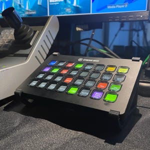 May include: A black Stream Deck with a grid of 32 customizable buttons. The buttons have various colored labels, including green, red, yellow, and blue. The Stream Deck is a popular tool for live streamers and content creators.