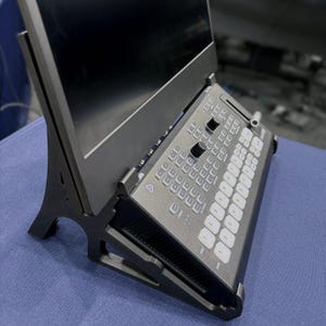 May include: A black video production switcher with a built-in monitor. The switcher has numerous buttons, knobs, and a fader. The monitor is angled for easy viewing. The device is designed for live video production and editing.
