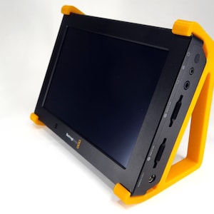 May include: A black portable monitor with a bright orange stand. The monitor has a screen with a black bezel and a small speaker on the right side. The stand is made of plastic and has a triangular shape.