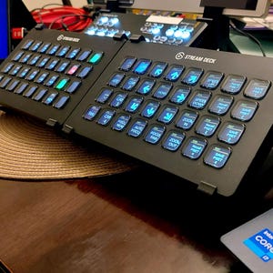 May include: A black Stream Deck with a grid of 32 customizable buttons. The buttons are illuminated with blue light and have various icons and text labels, including "Speed Up", "Zoom In", "Save Preset", and "Focus Auto".