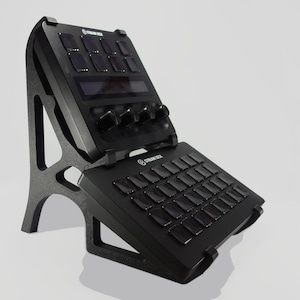 May include: A black Stream Deck device with multiple buttons, knobs, and a screen, mounted on a black stand. The device is designed for content creation and streaming, with a sleek, modern design. The stand provides an angled, ergonomic setup.