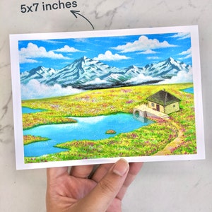 May include: A watercolour painting of a small house with a blue roof, nestled in a green field with a blue lake. The house is surrounded by mountains in the background, and the sky is blue with white clouds.