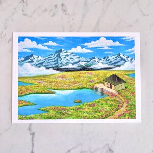May include: A painting depicting a small cottage with a brown roof and a blue door, set in a field of green grass and pink flowers. The cottage is close to a small blue lake, with a mountain range in the background. The sky is blue with white clouds.