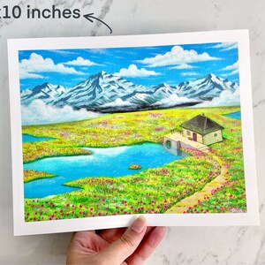 May include: An 8x10 inch print of a watercolour painting depicting a small cottage with a water wheel in a field of flowers. The cottage is surrounded by a blue lake and snow-capped mountains in the background.