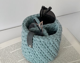 Puede incluir: Un organizador de crochet azul claro con dos pares de gafas de sol en su interior. El organizador tiene una correa de cuero con la palabra "CAPTOYANPED" impresa en ella.