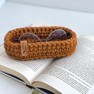 These photo shows a small oval-shaped knitted tray. On the side of the tray is a leather tag with the inscription "Made with love".