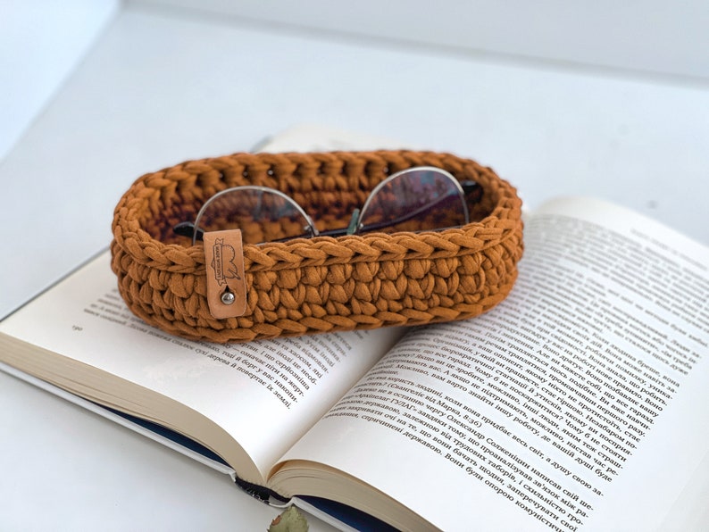 These photo shows a small oval-shaped knitted tray. On the side of the tray is a leather tag with the inscription "Made with love".