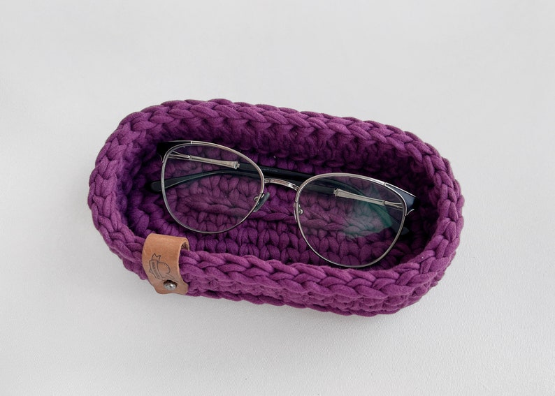 The photo shows a small oval-shaped knitted tray. On the side of the tray is a leather tag with the inscription "Made with love".