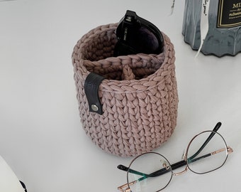 Puede incluir: Un organizador de crochet de color marrón claro con una correa de cuero negro y una hebilla de metal. Dos pares de gafas están en el organizador.