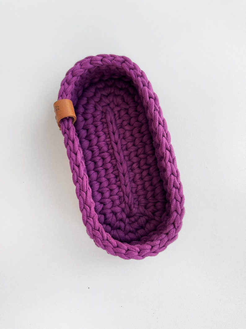 The photo shows a small oval-shaped knitted tray. On the side of the tray is a leather tag with the inscription "Made with love".