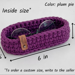 The photo shows a small oval-shaped knitted tray. On the side of the tray is a leather tag with the inscription "Made with love".