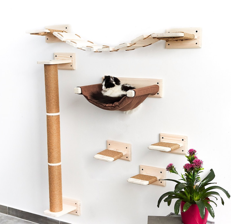 Pode incluir: Uma &aacute;rvore para gatos com uma variedade de plataformas e uma rede para os gatos relaxarem. A &aacute;rvore para gatos &eacute; feita de madeira e tem um acabamento natural. A &aacute;rvore para gatos est&aacute; montada em uma parede branca.