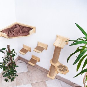 May include: A wooden cat tree with a bed, scratching post, and multiple platforms. The cat tree is mounted on a white wall and has a brown cushion in the bed.