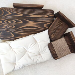 May include: A set of three wooden cat scratching posts with a beige cushion. The posts are made of dark wood and have a natural finish. The cushion is made of a soft, plush fabric.
