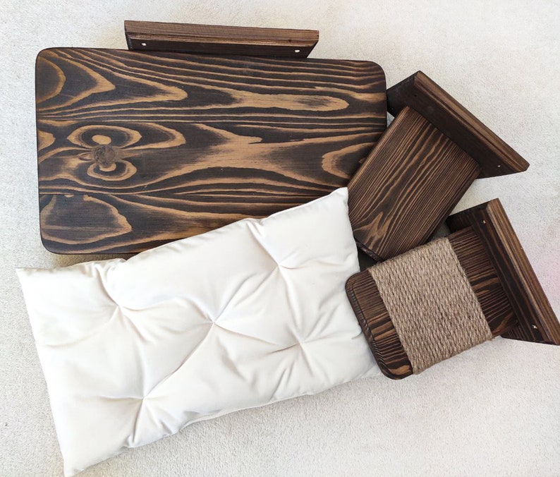 May include: A set of three wooden cat scratching posts with a beige cushion. The posts are made of dark wood and have a natural finish. The cushion is made of a soft, plush fabric.