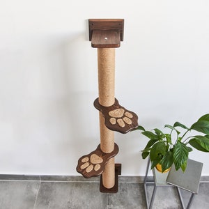 May include: A brown wooden cat scratching post with three platforms. The platforms are shaped like paw prints and are covered in sisal rope. The post is mounted to a wall.