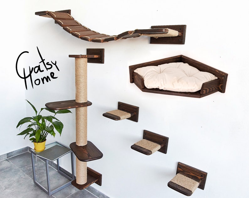 May include: A wooden cat tree with a scratching post, multiple platforms, and a bridge. The cat tree is mounted on a white wall. The cat tree is made of dark brown wood and has a natural rope scratching post. The cat tree also includes a hammock-style bed with a white cushion.