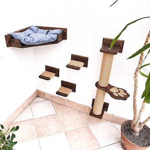 May include: A wooden cat tree with a scratching post, a bed, and multiple platforms. The cat tree is mounted on a white wall. A potted plant is in the lower right corner of the image.